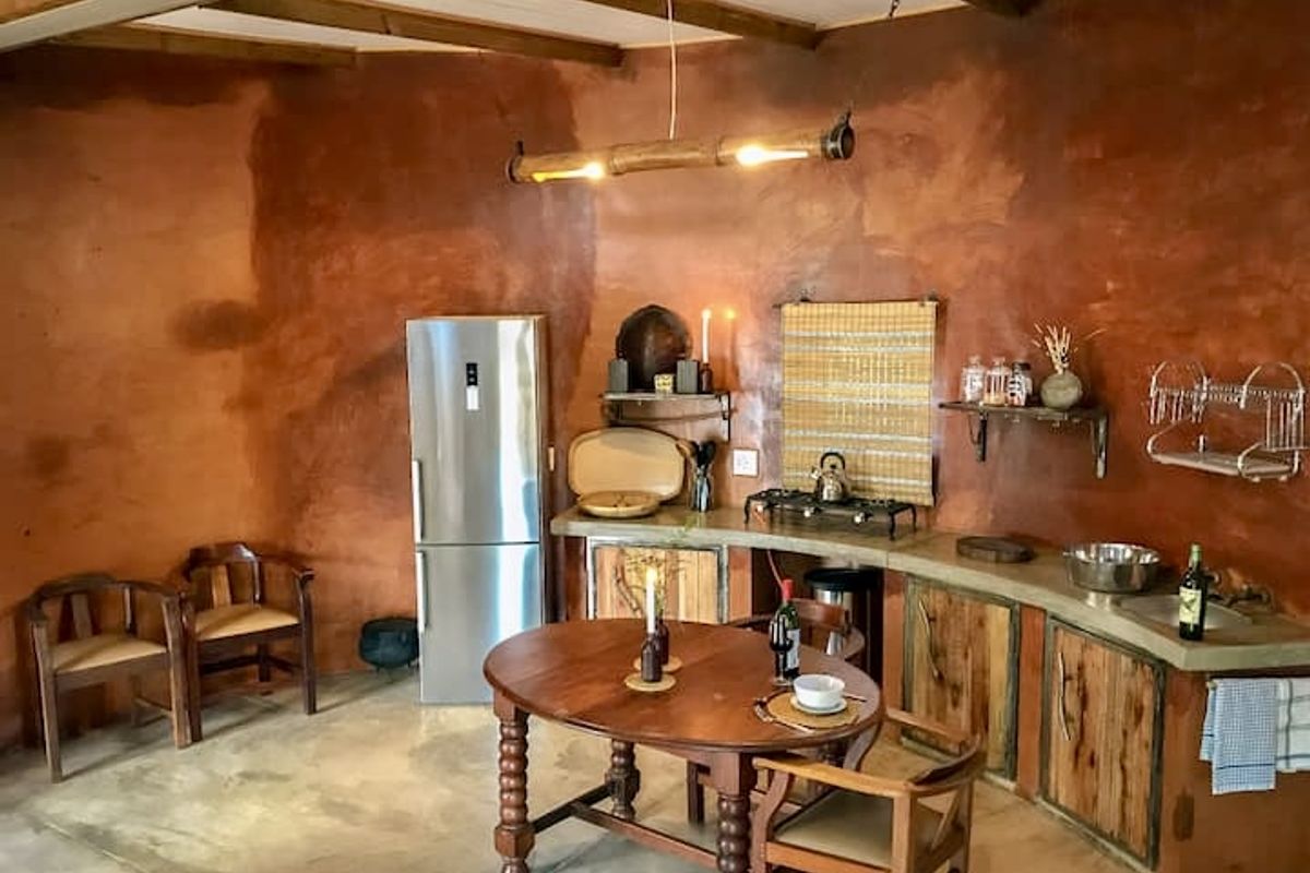 Rustic kitchen featuring textured terracotta-toned walls, exposed timber ceiling beams, concrete countertops, and custom wooden cabinetry with integrated sink and gas hob.