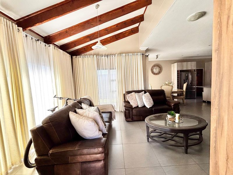 Spacious open-plan living area featuring exposed timber ceiling beams, tiled flooring, and a seamless flow into the adjacent kitchen and dining space.