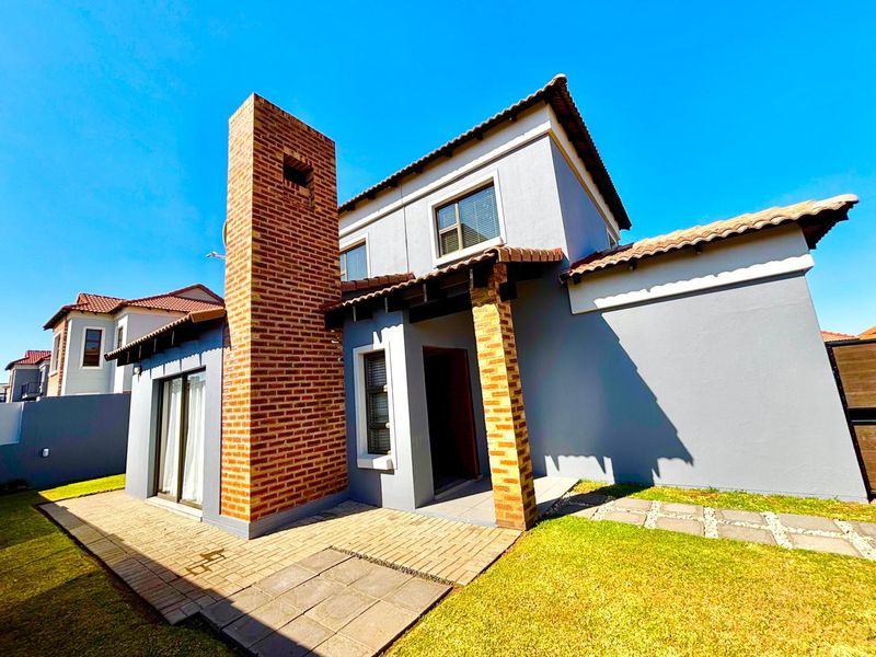 Rear view of the townhouse featuring a paved patio area, prominent brick chimney, and well-maintained exterior walls with tiled roofing.