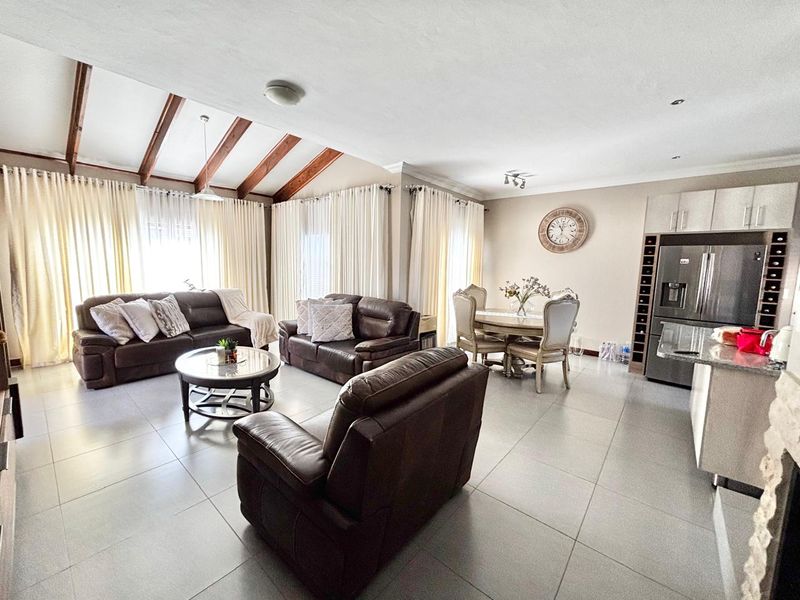 Spacious open-plan living and dining area featuring exposed timber ceiling beams, large windows with natural light, and a modern kitchen with granite countertops.