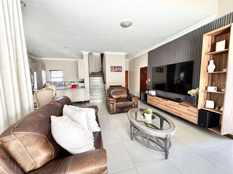 Spacious open-plan living area featuring tiled floors, a modern slatted feature wall, and an integrated kitchen with a central island and staircase access.