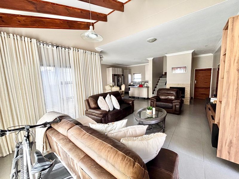 Spacious open-plan living area featuring exposed timber ceiling beams, tiled flooring, a built-in fireplace, and a seamless flow into the kitchen space.