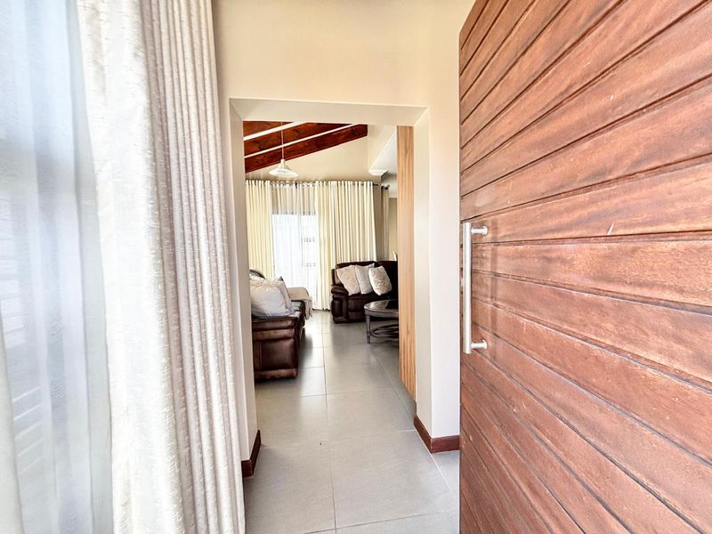 Entrance foyer featuring a solid timber door, neutral tiled flooring, and a view through to the living area with exposed timber ceiling beams.