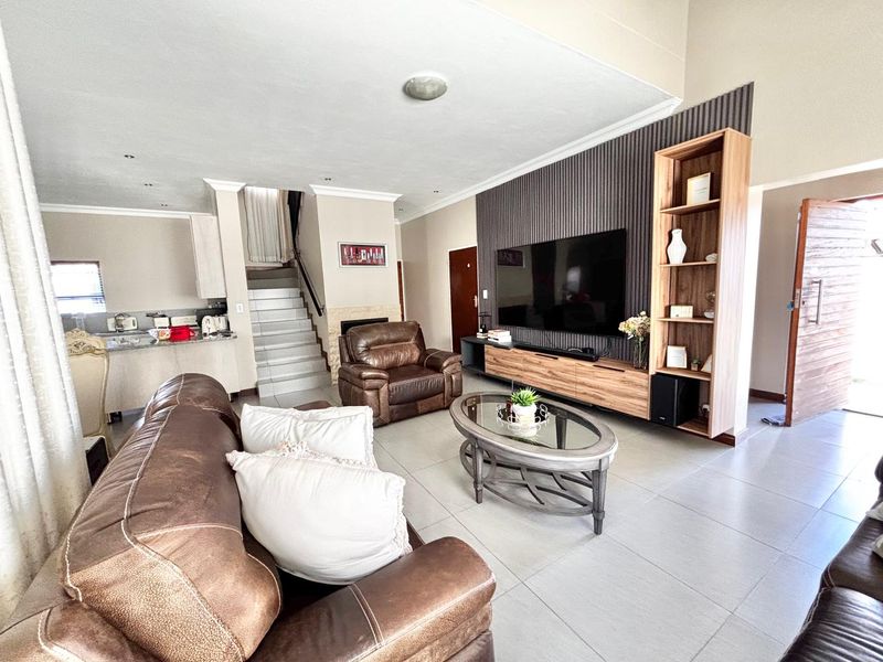 Spacious open-plan living area featuring tiled floors, a modern feature wall with built-in cabinetry, and an integrated staircase leading to the upper level.