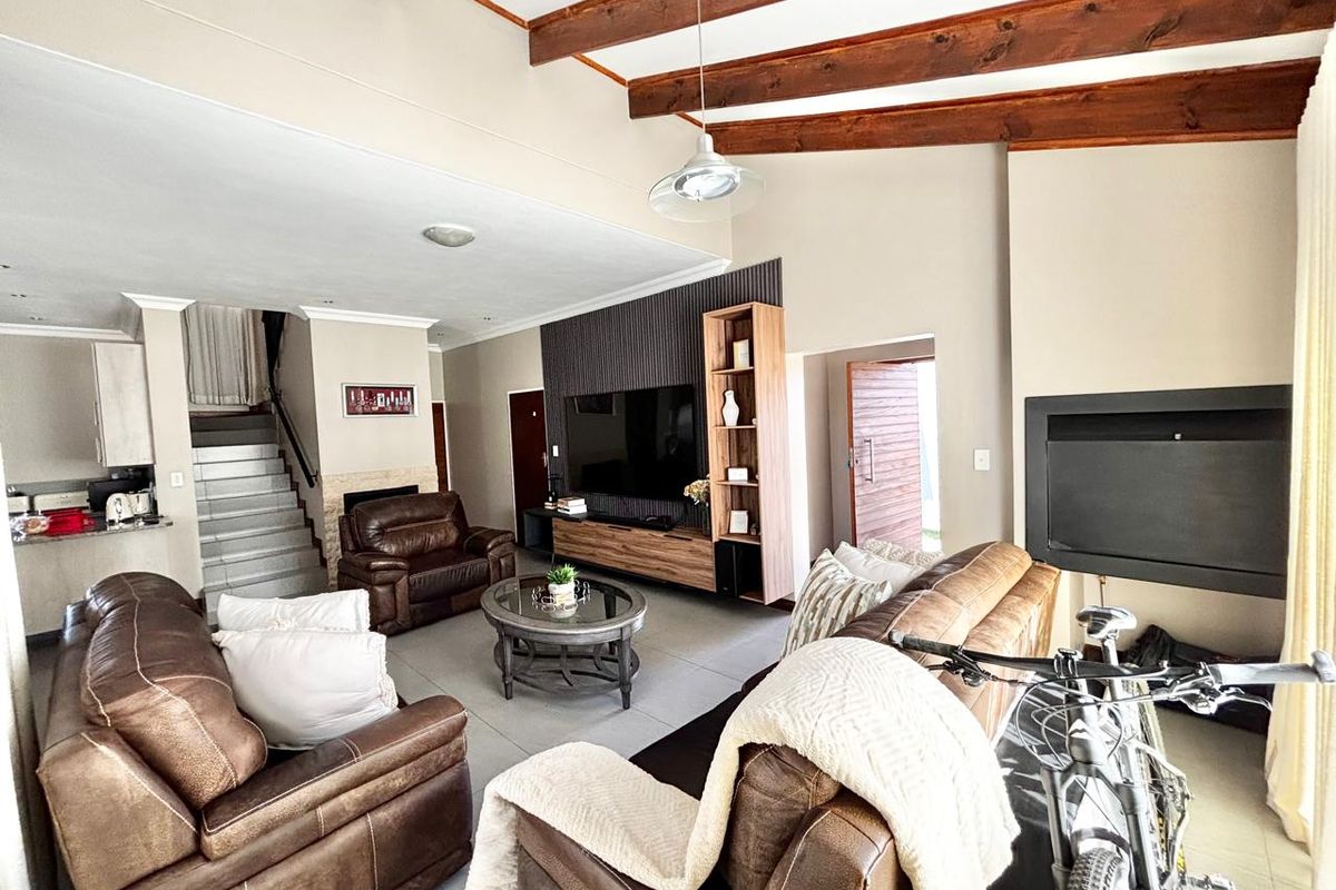 Spacious living room featuring exposed timber ceiling beams, a built-in fireplace, and a feature wall, with an open-plan layout leading to a staircase.