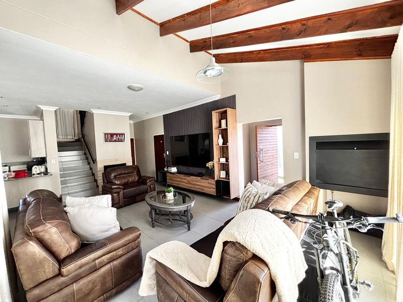 Spacious living room featuring exposed timber ceiling beams, a built-in fireplace, and a feature wall, with an open-plan layout leading to a staircase.