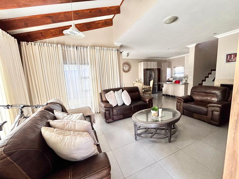Spacious open-plan living area featuring exposed timber ceiling beams, tiled flooring, and a modern kitchen with a central island and built-in cabinetry.