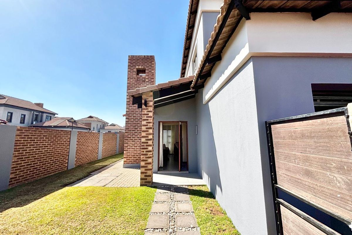 Rear view of the townhouse featuring a brick chimney, paved walkway, and a private garden area with a brick boundary wall.