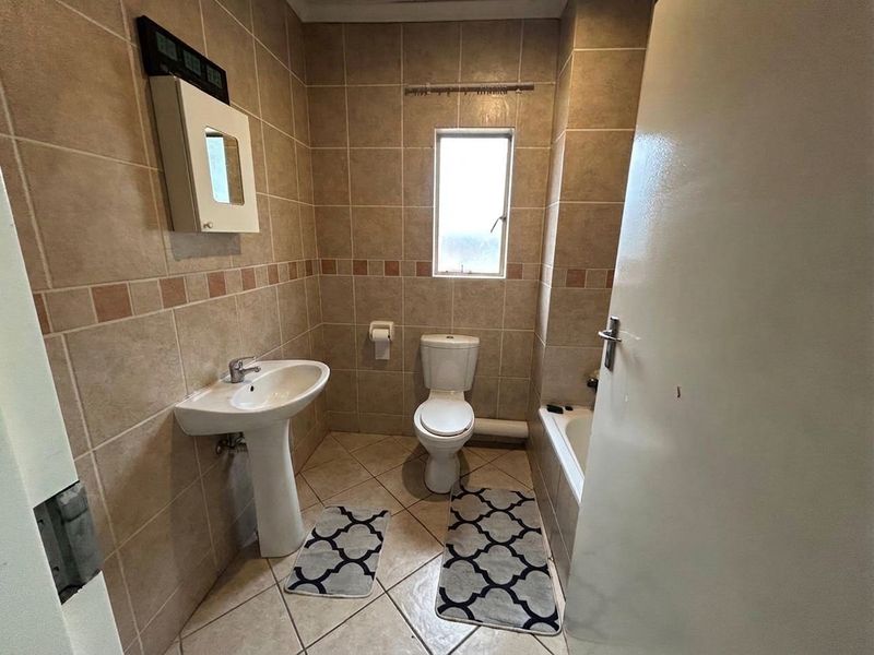 A functional bathroom featuring a pedestal basin, toilet, and bathtub with neutral wall and floor tiling.