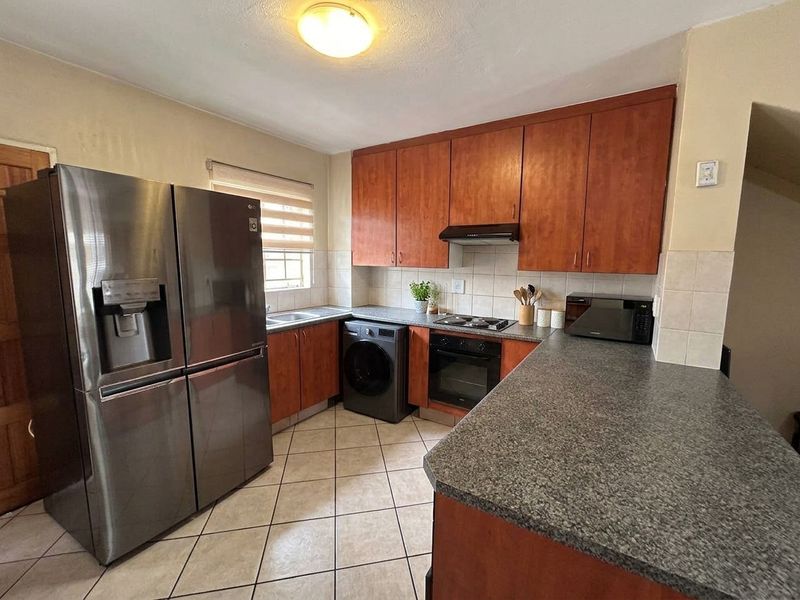 Functional kitchen featuring wood-finish cabinetry, granite-look countertops, tiled backsplash, and integrated cooking appliances with tiled flooring.