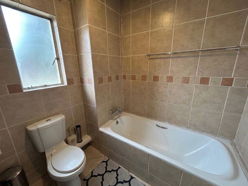 A functional bathroom featuring a built-in bathtub, toilet, and neutral wall tiling with a frosted window for natural light.