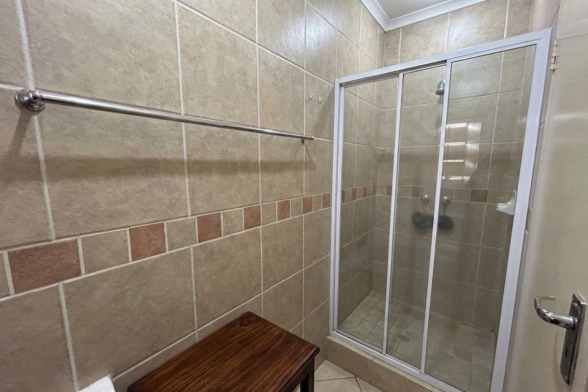 A functional bathroom featuring a tiled shower enclosure with sliding glass doors and neutral wall tiling.