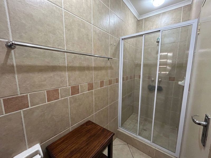A functional bathroom featuring a tiled shower enclosure with sliding glass doors and neutral wall tiling.
