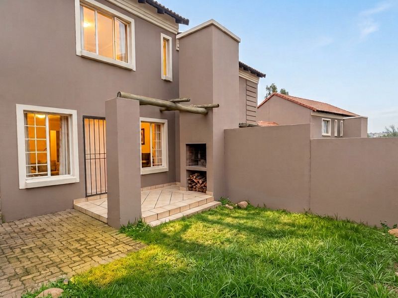 Rear exterior view of the townhouse featuring a paved patio, built-in braai, timber pergola, and a private garden area with perimeter walling.