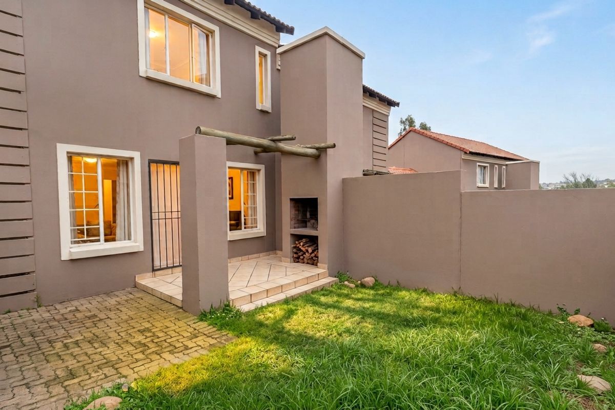 Rear exterior view of the townhouse featuring a paved patio, built-in braai, timber pergola, and a private garden area with perimeter walling.