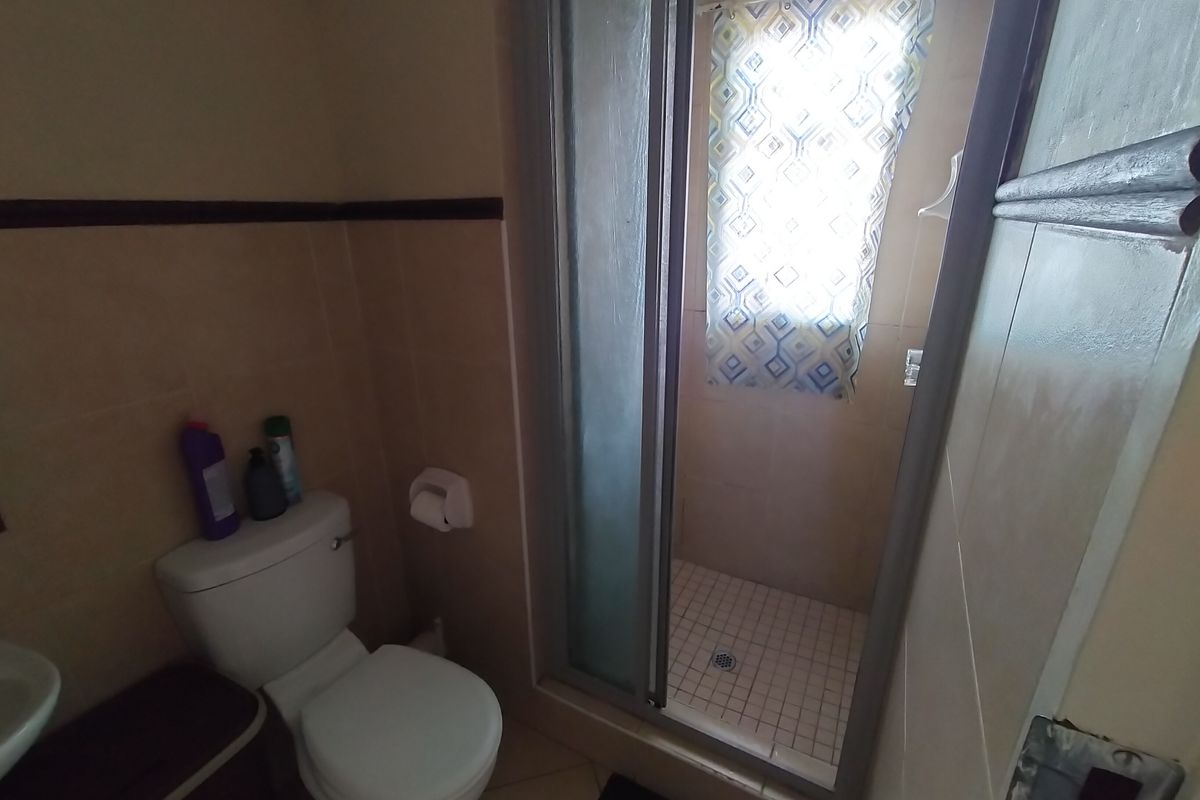 A compact bathroom featuring a shower enclosure, toilet, and tiled finishes, requiring some maintenance and cosmetic updates.