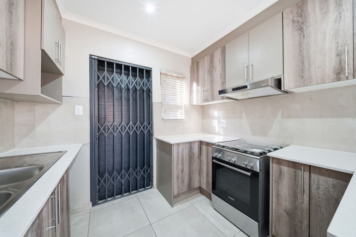 Modern kitchen featuring wood-look cabinetry, stone-style countertops, tiled backsplash, and a stainless steel oven with extractor fan, leading to a secure exterior door.