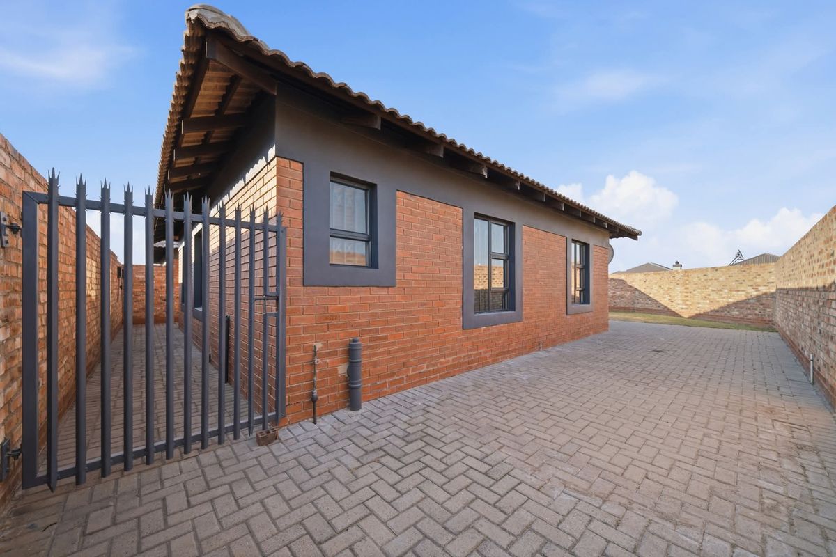 A well-maintained rear exterior view of a face brick house featuring a paved driveway, secure perimeter walling, and modern aluminium window frames.