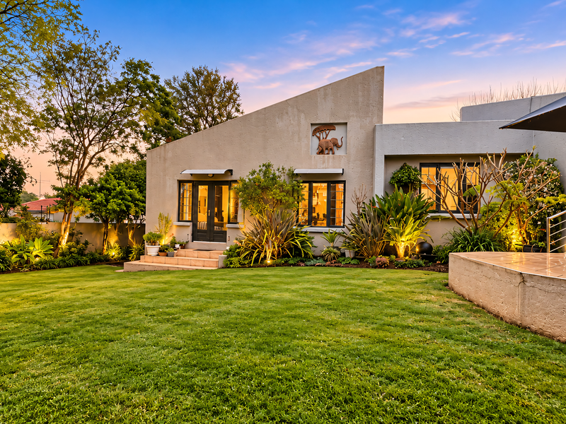 A beautifully landscaped rear garden featuring a well-maintained lawn, mature plantings, and a spacious tiled patio area attached to the modern townhouse.