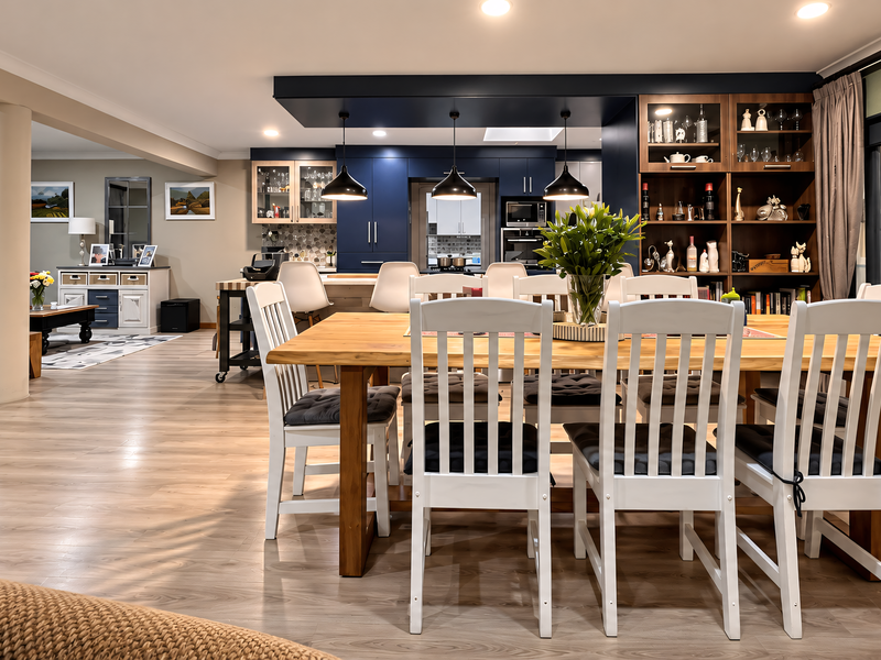 Spacious open-plan living and dining area featuring modern kitchen cabinetry, built-in shelving, laminate flooring, and seamless access to the outdoor patio.