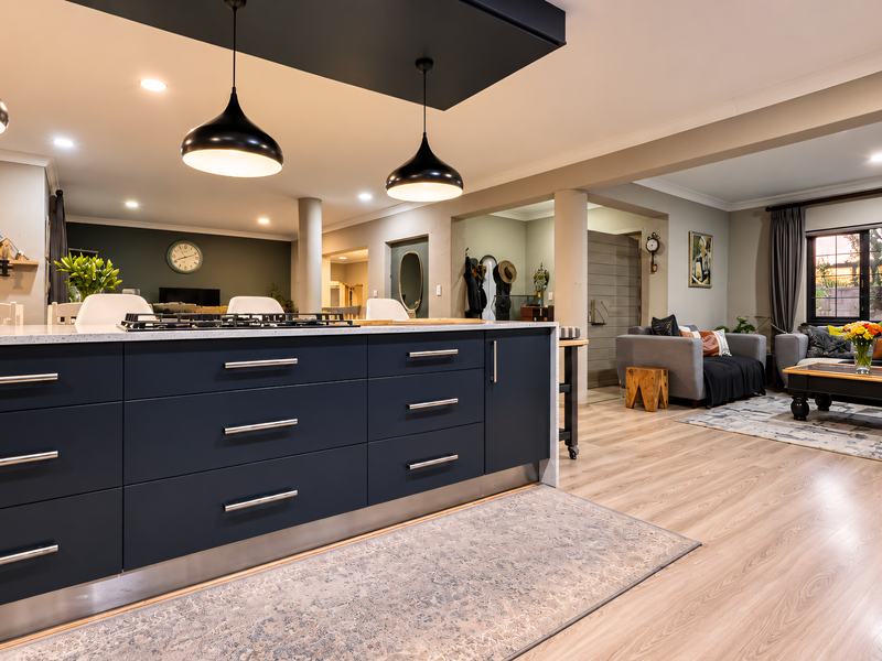 Spacious open-plan living area featuring a modern kitchen island with a gas cooktop, pendant lighting, and light-toned laminate flooring throughout.