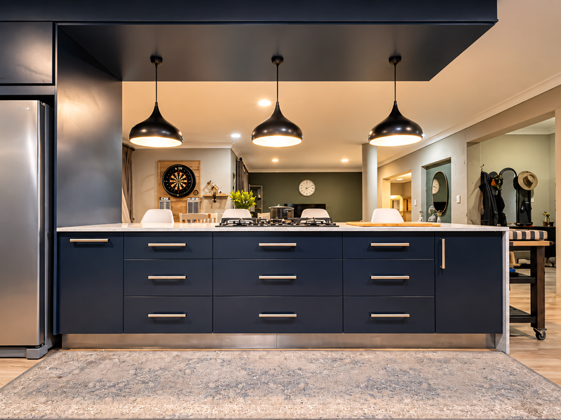 Modern open-plan kitchen featuring a large navy blue island with stone countertops, gas cooktop, and stylish pendant lighting, seamlessly flowing into the living area.