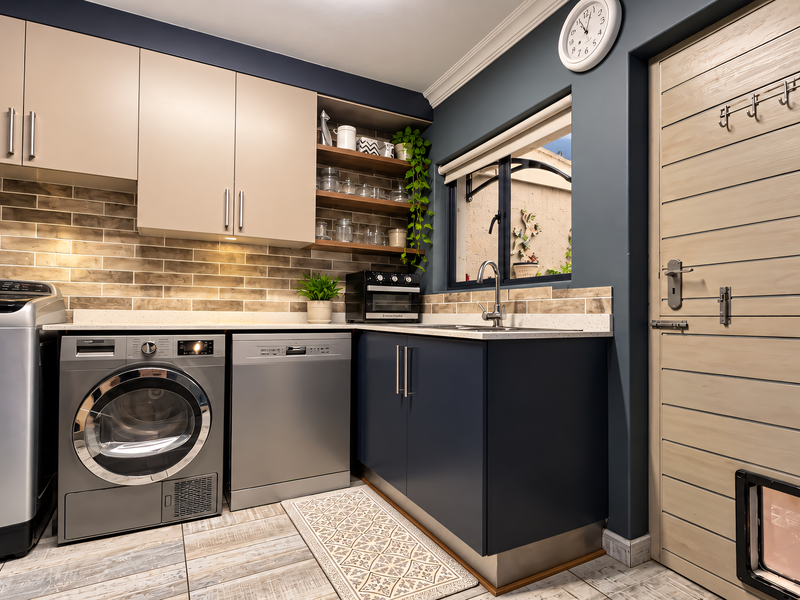 Modern, well-appointed laundry room featuring sleek cabinetry, subway tile backsplash, stainless steel sink, and integrated appliance spaces with a convenient pet door.