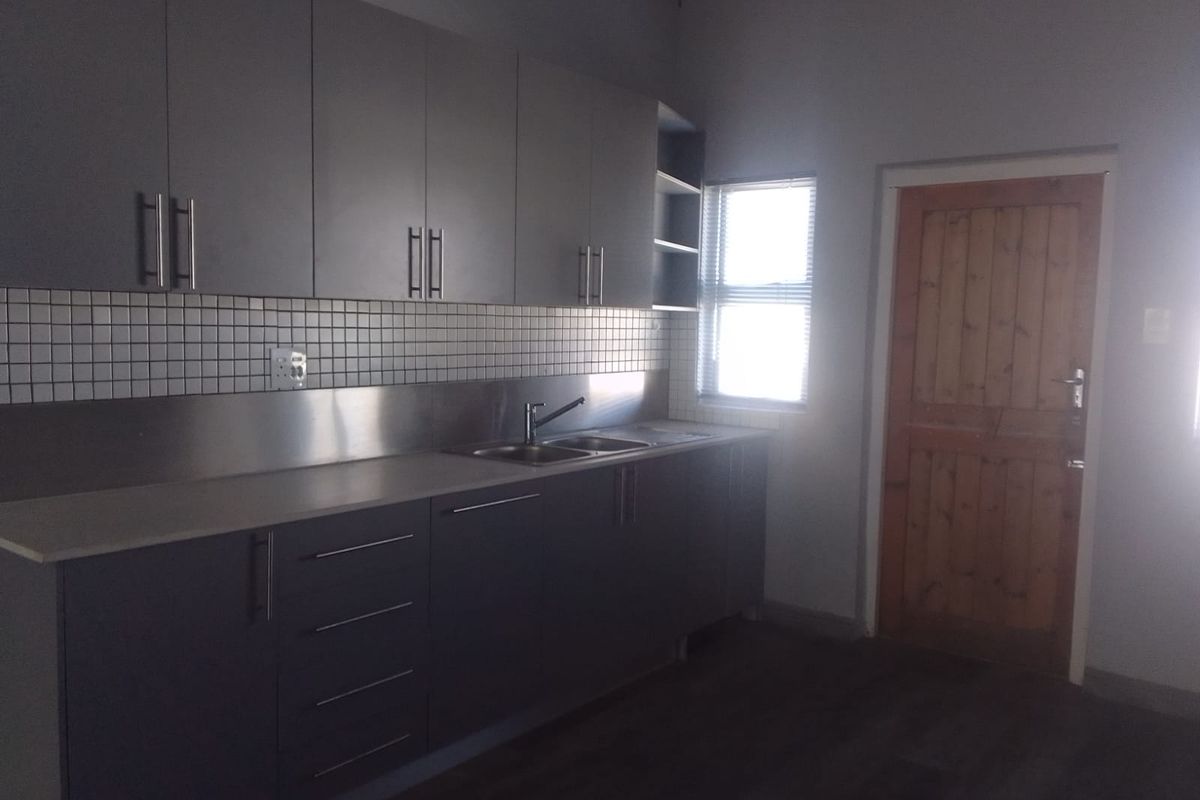 A functional kitchen featuring modern grey cabinetry, a stainless steel sink, tiled backsplash, and a wooden door leading to the exterior.
