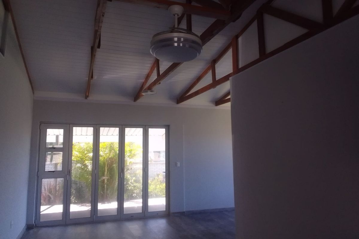 Spacious living area featuring exposed timber roof trusses, vaulted ceilings, and large glass folding doors providing direct access to the garden.