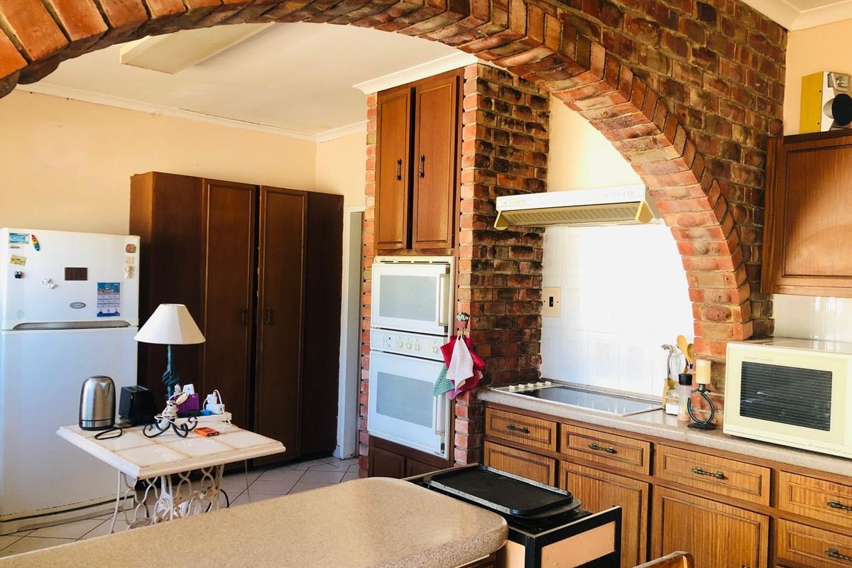 A traditional kitchen featuring wooden cabinetry, a built-in oven, an electric hob with extractor fan, and a distinctive brick archway.