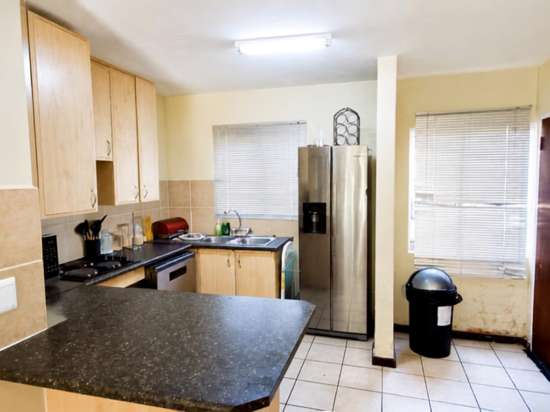A functional kitchen featuring laminate cabinetry, dark countertops, tiled flooring, and a built-in hob, requiring some cosmetic updates to the walls.