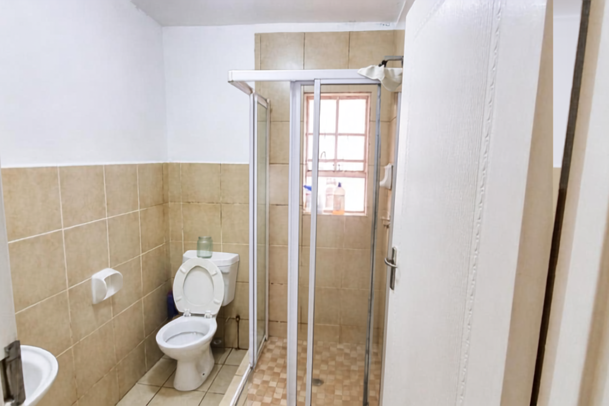 A functional bathroom featuring a shower enclosure, toilet, and neutral wall tiling, offering a clean and practical space.