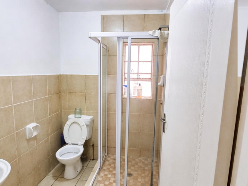 A functional bathroom featuring a shower enclosure, toilet, and neutral wall tiling, offering a clean and practical space.