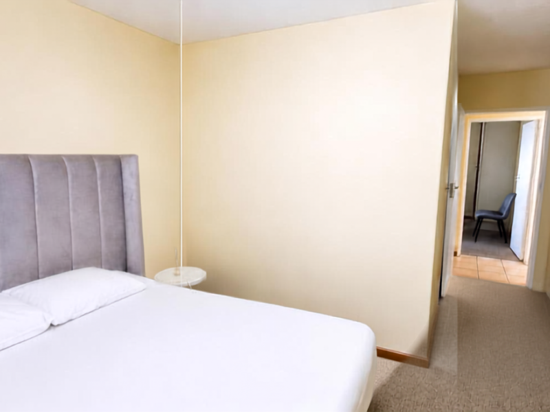 A bedroom featuring neutral walls, carpeted flooring, and built-in storage cupboards, with a view leading into an adjacent hallway.