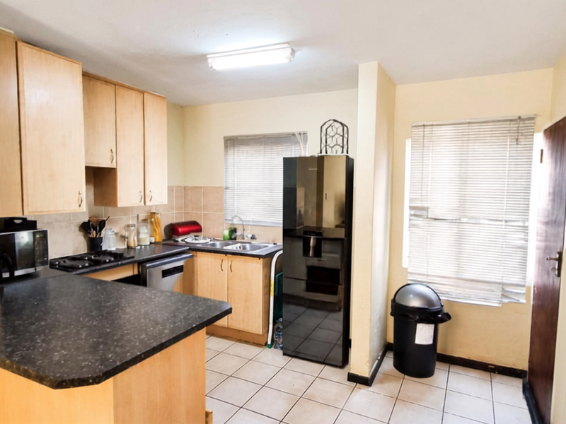 A functional kitchen featuring laminate cabinetry, dark countertops, ceramic tile flooring, and a double bowl sink with natural light from window blinds.