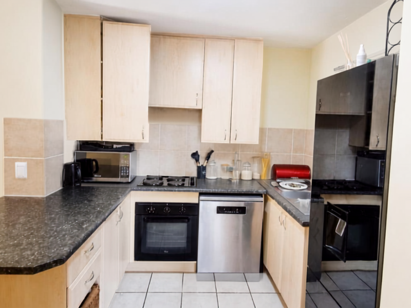 Functional kitchen featuring light wood cabinetry, dark laminate countertops, tiled backsplash, built-in oven, gas hob, and stainless steel dishwasher.