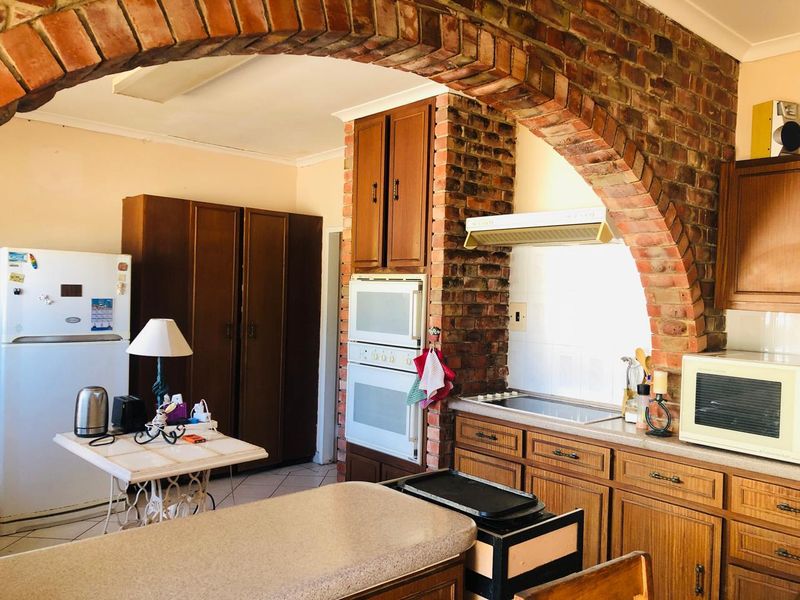 A traditional kitchen featuring wooden cabinetry, a built-in oven, an electric hob with extractor fan, and a distinctive brick archway.