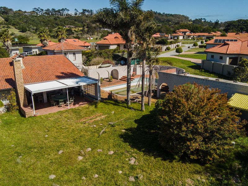 Aerial view of a residential property featuring a tiled roof, covered patio, swimming pool, and surrounding garden area within a suburban estate.