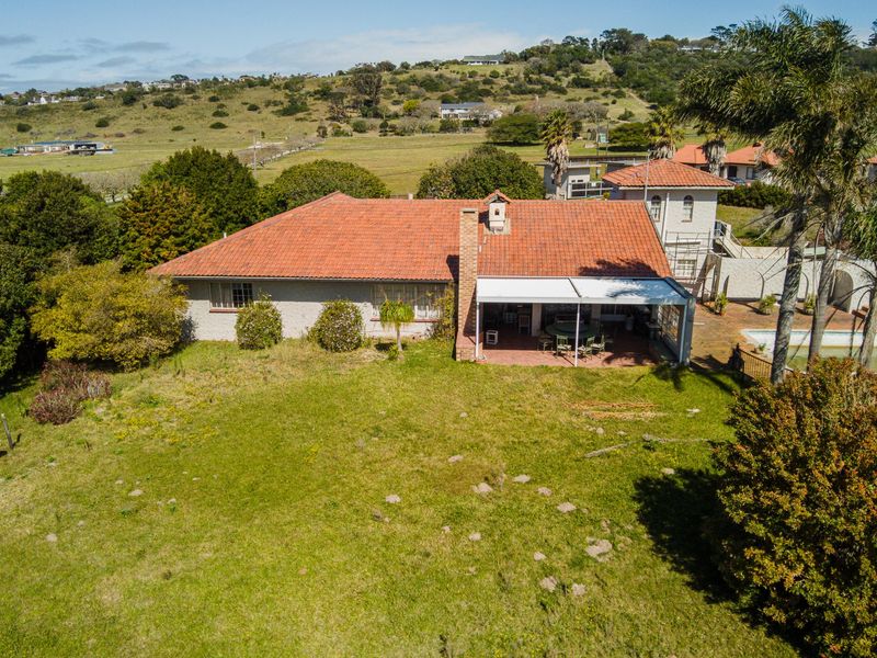 Aerial view of a residential property featuring a tiled roof, a covered patio area, and a spacious surrounding garden with scenic landscape views.