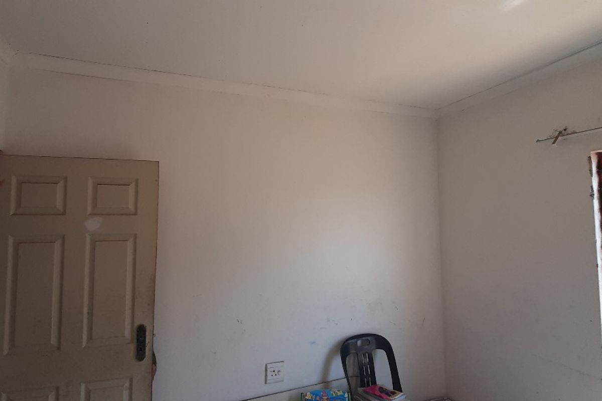 A simple bedroom featuring white walls, a window with security bars, and a standard interior door.