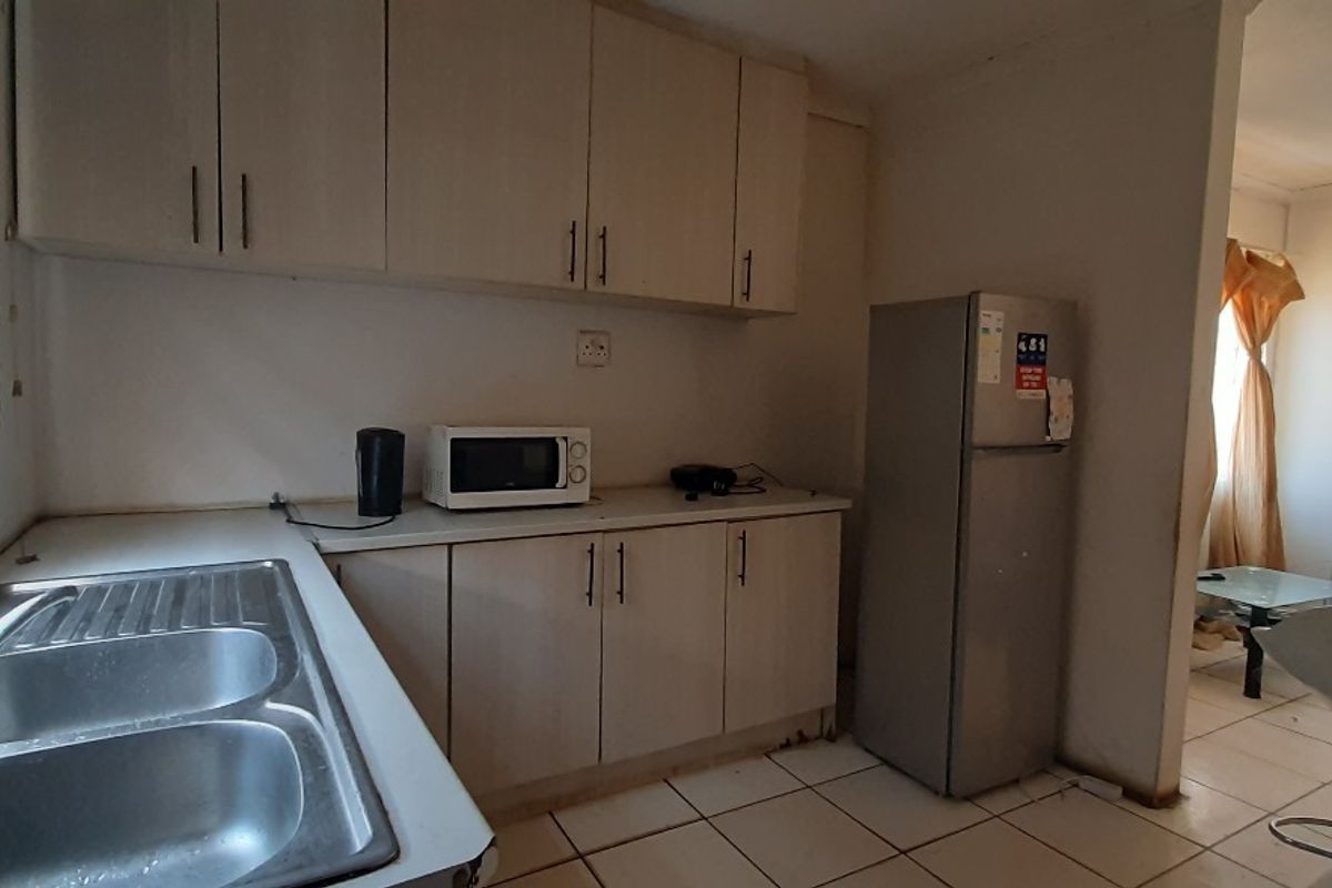 A functional kitchen featuring laminate cabinetry, a double bowl stainless steel sink, and tiled flooring, offering potential for modernization.
