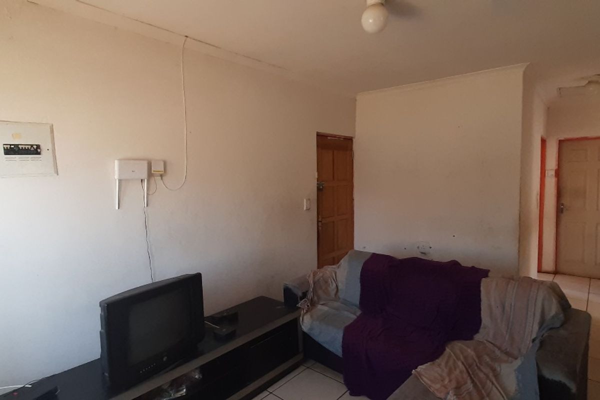 A living room area featuring tiled flooring and a wall-mounted electrical distribution board, requiring cosmetic updates to improve the overall aesthetic.
