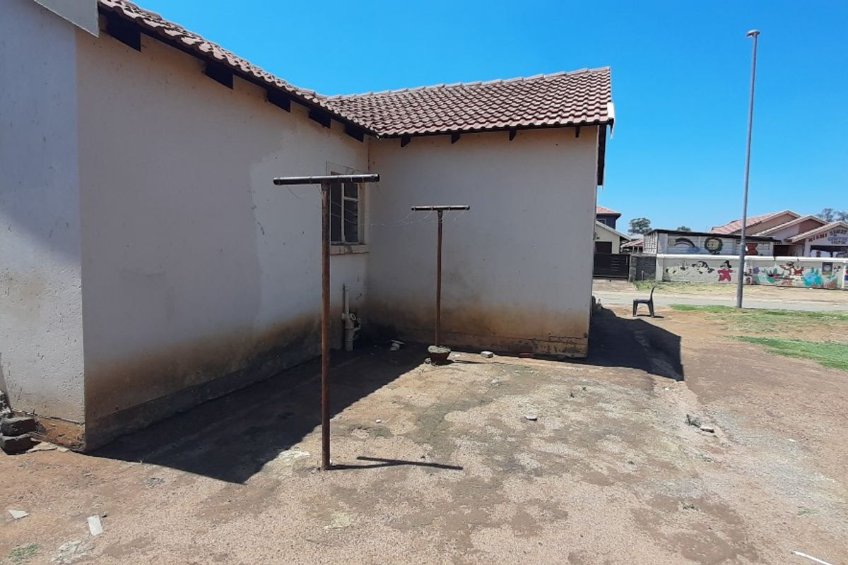 Rear exterior view of the property showing tiled roofing, metal washing line poles, and significant signs of rising damp and plaster deterioration on the walls.