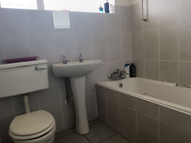 A functional bathroom featuring a pedestal basin, built-in bathtub, and toilet with neutral wall and floor tiling.