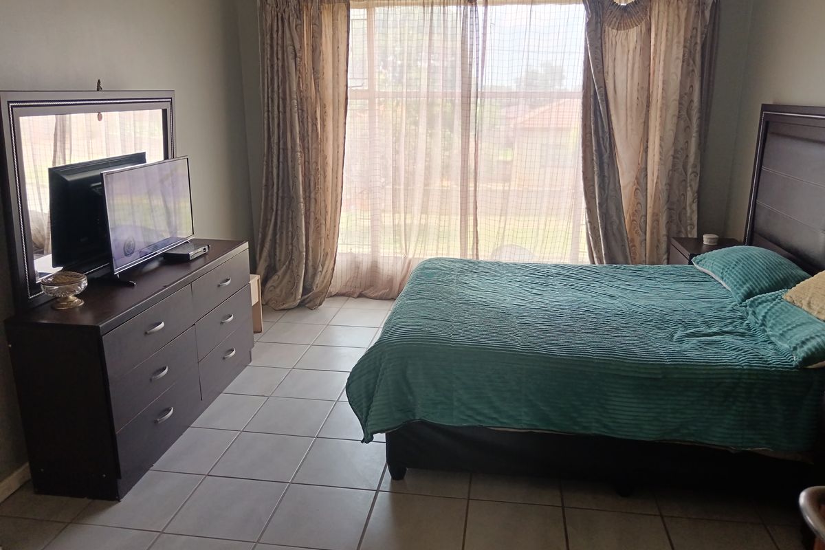 A spacious bedroom featuring neutral tiled flooring and a large window with curtain tracks, providing natural light and access to the exterior.