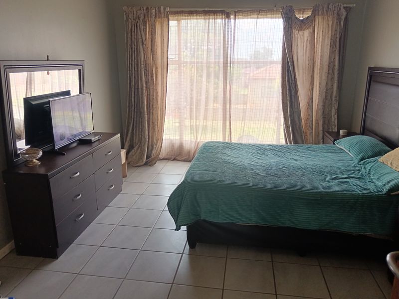 A spacious bedroom featuring neutral tiled flooring and a large window with curtain tracks, providing natural light and access to the exterior.