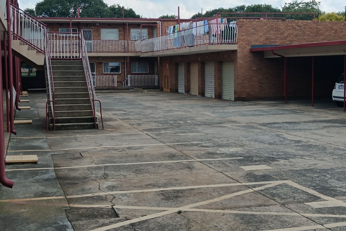 Rear exterior view of an apartment complex featuring a concrete staircase, paved parking area, and multiple garage units.