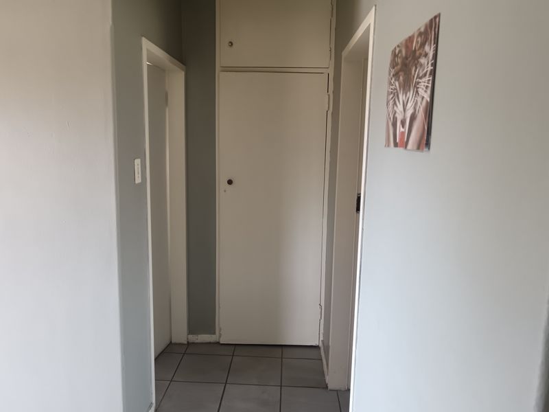 A functional hallway featuring tiled flooring and a built-in storage cupboard, providing access to adjacent rooms within the apartment.