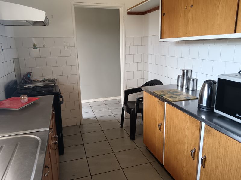 A functional kitchen featuring wooden cabinetry, stainless steel countertops, and tiled splashbacks, offering a dated aesthetic ready for modernization.