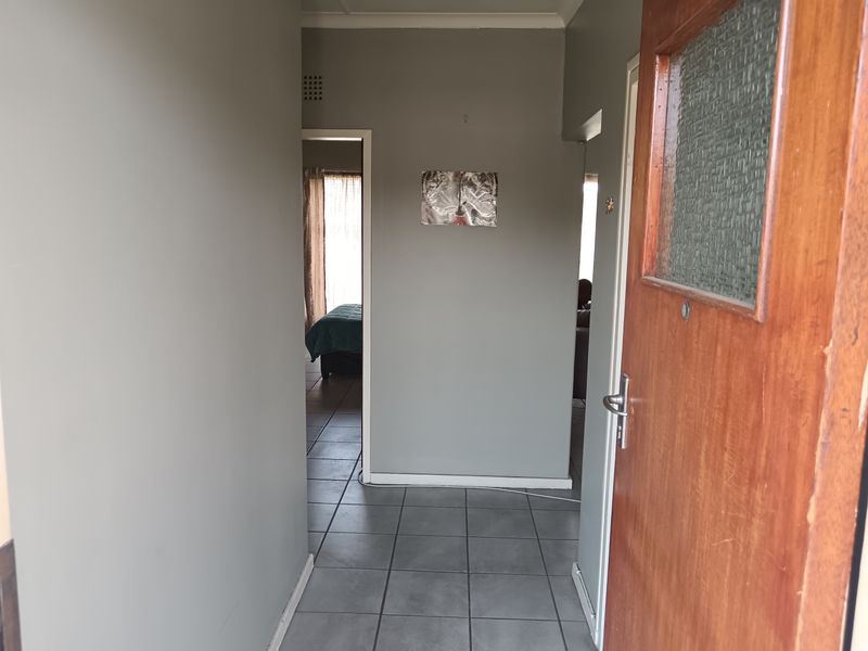 A functional hallway featuring tiled flooring and a wooden entrance door, providing access to adjacent rooms within the apartment.